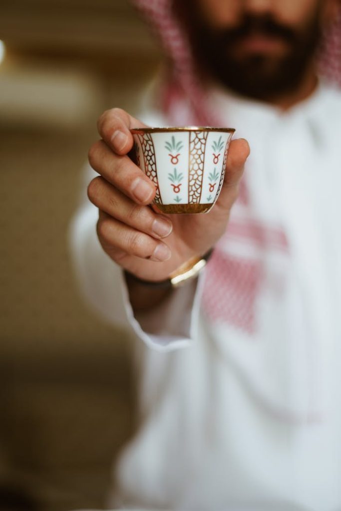 Close-up of Middle Eastern man in traditional attire offering a decorative cup of coffee.